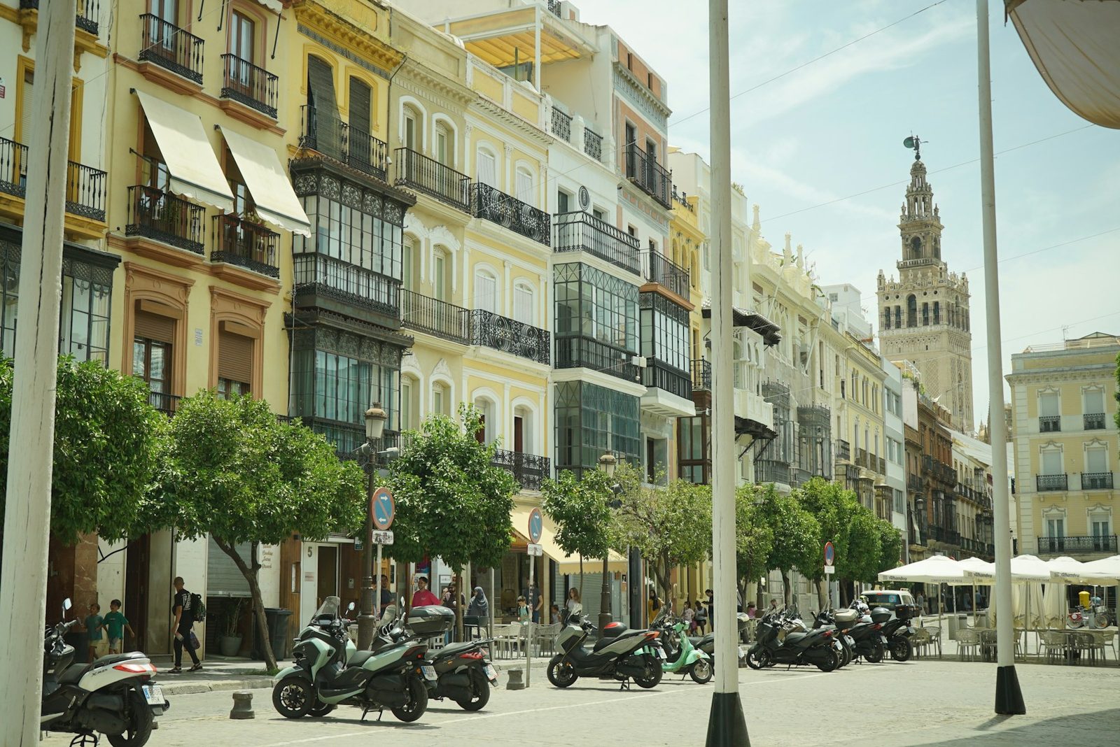 A historic street in Seville, Spain, orange trees and outdoor cafes lining the facades.