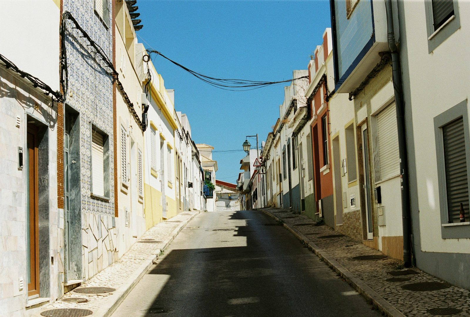 An empty side street of pastel, tile-fronted buildings in an old town in the Algarve, Portugal.